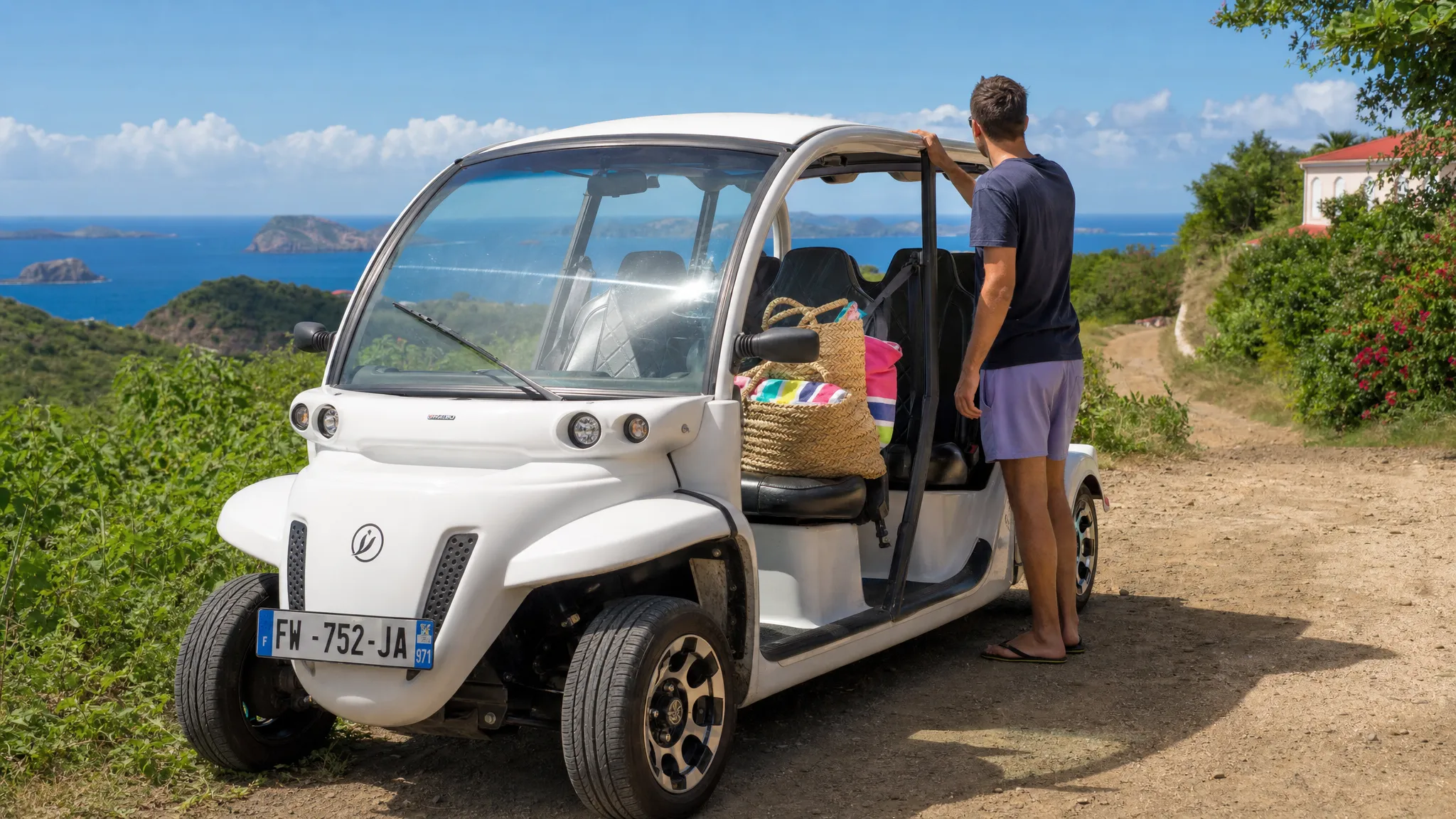 Une voiturette électrique garée au bord d’un chemin de Terre-de-Haut, avec un adulte à côté du véhicule, des sacs de plage visibles sur la banquette et la mer au loin.